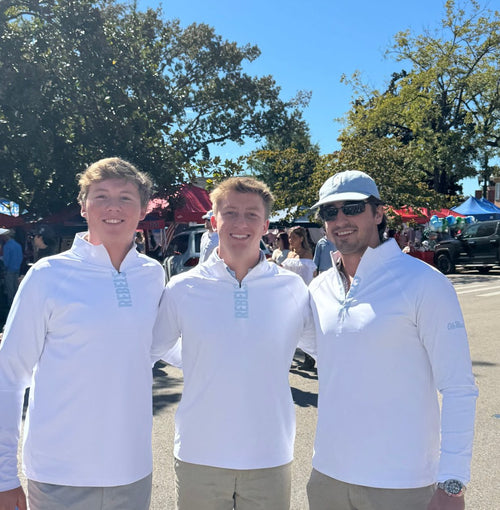 Three Ole Miss Rebels fans wearing GMDY white quarter zips with light blue REBELS lettering on game day